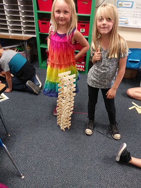 two students standing next to something they build with wood planks 
