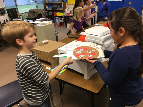 a student handing another student a pizza made of paper